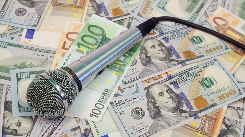 Header image: a microphone resting on a carpet of $100 bills (credit: ZhdanHenn / Shutterstock.com)