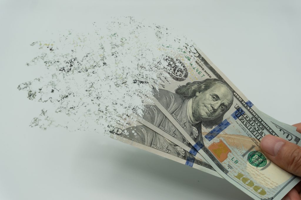 Header image: hand holding a sheaf of $100 bills that are disintegrating and flying away (Credit: evan_huang / Shutterstock.com)