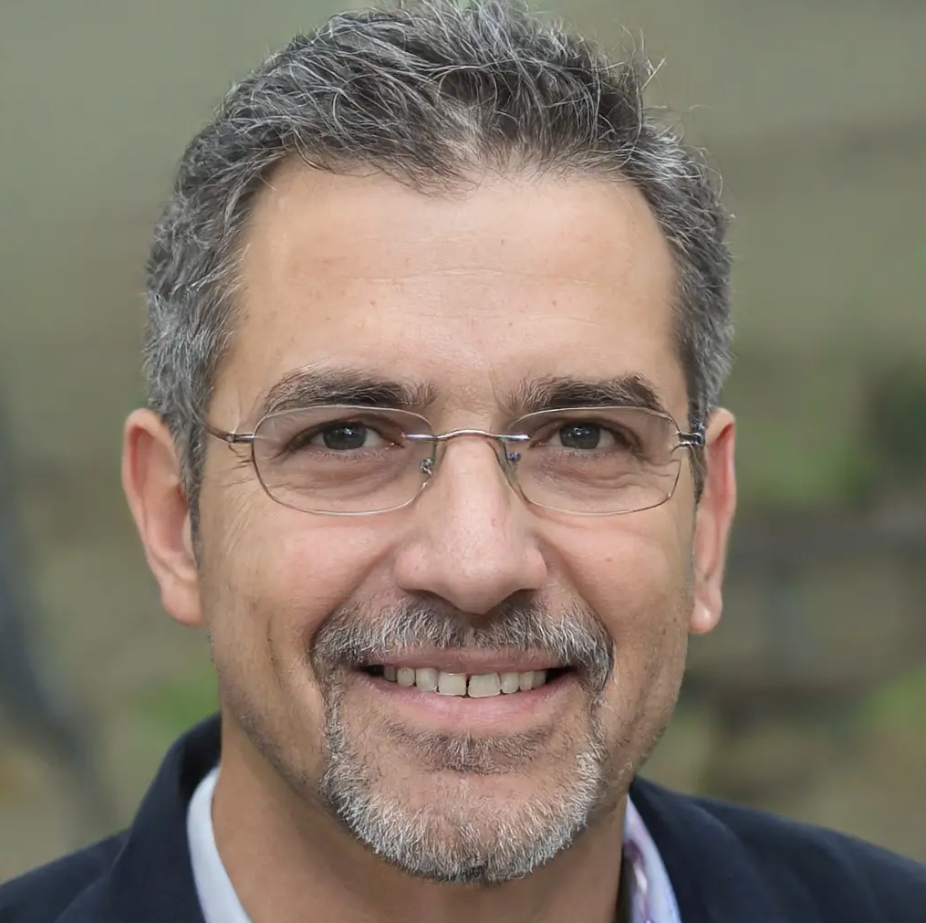 Image of "Denise Clark": older man with  glasses, gray hair, gray beard, and navy jacket, with a blurred background. 